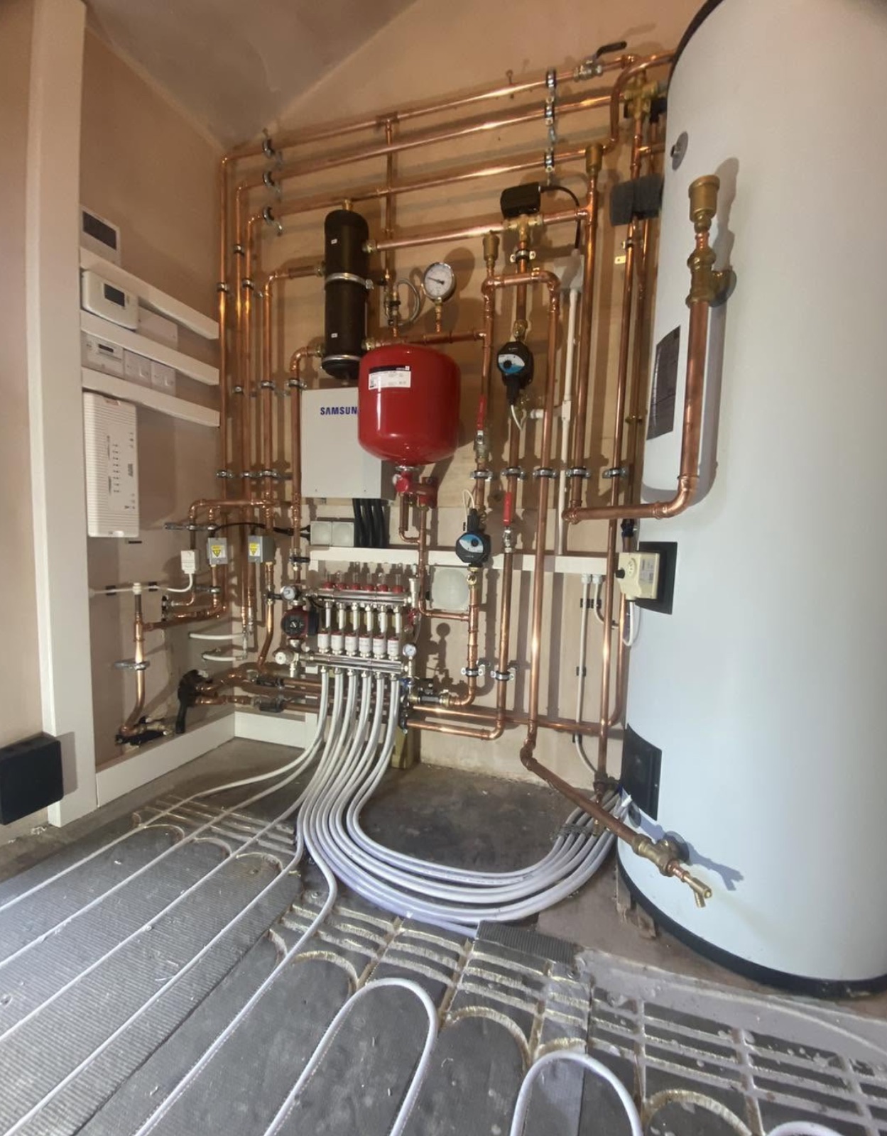 Heat pump plant room with copper pipework and underfloor heating manifold