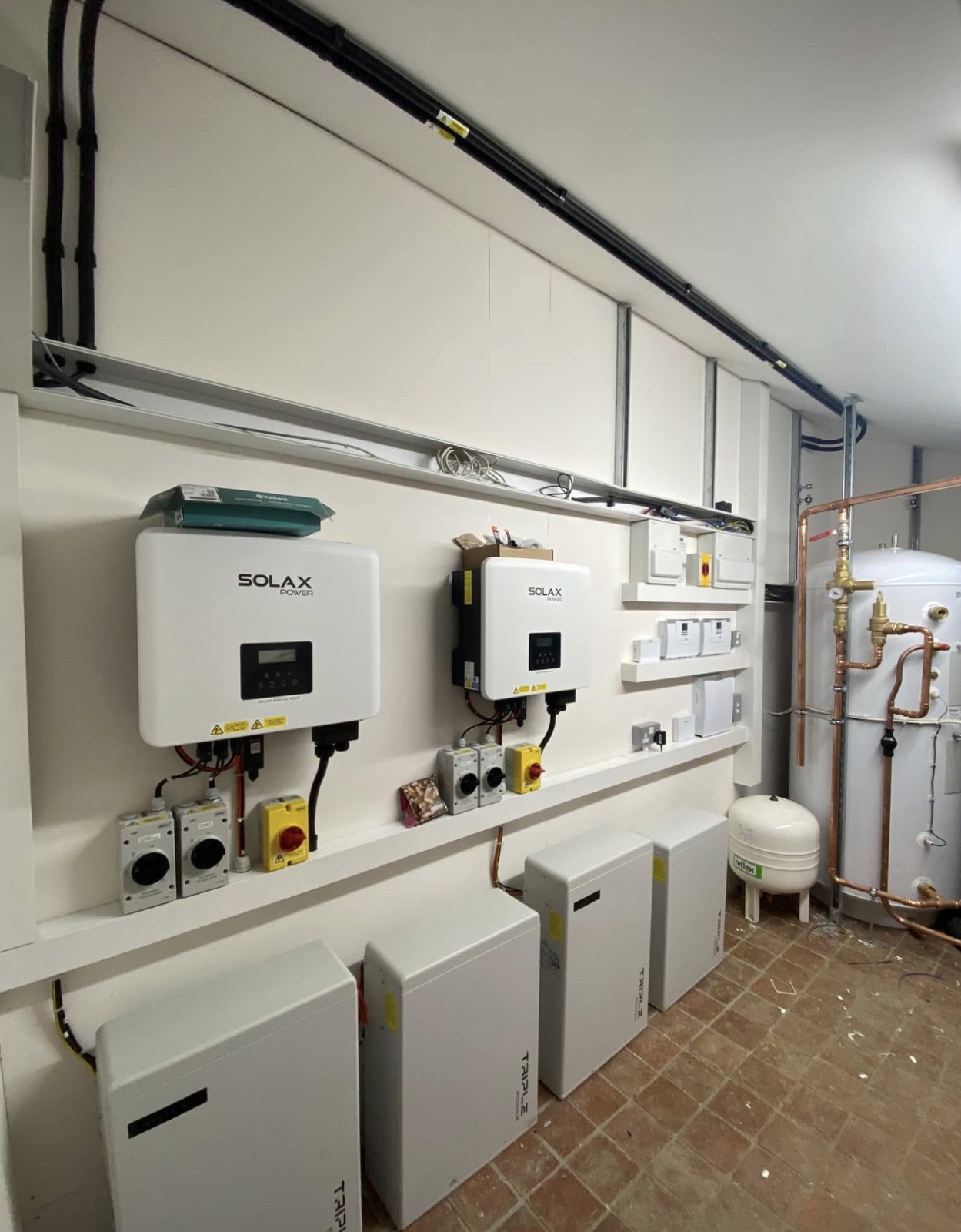 Solar inverters, isolators and battery storage on a plant room wall