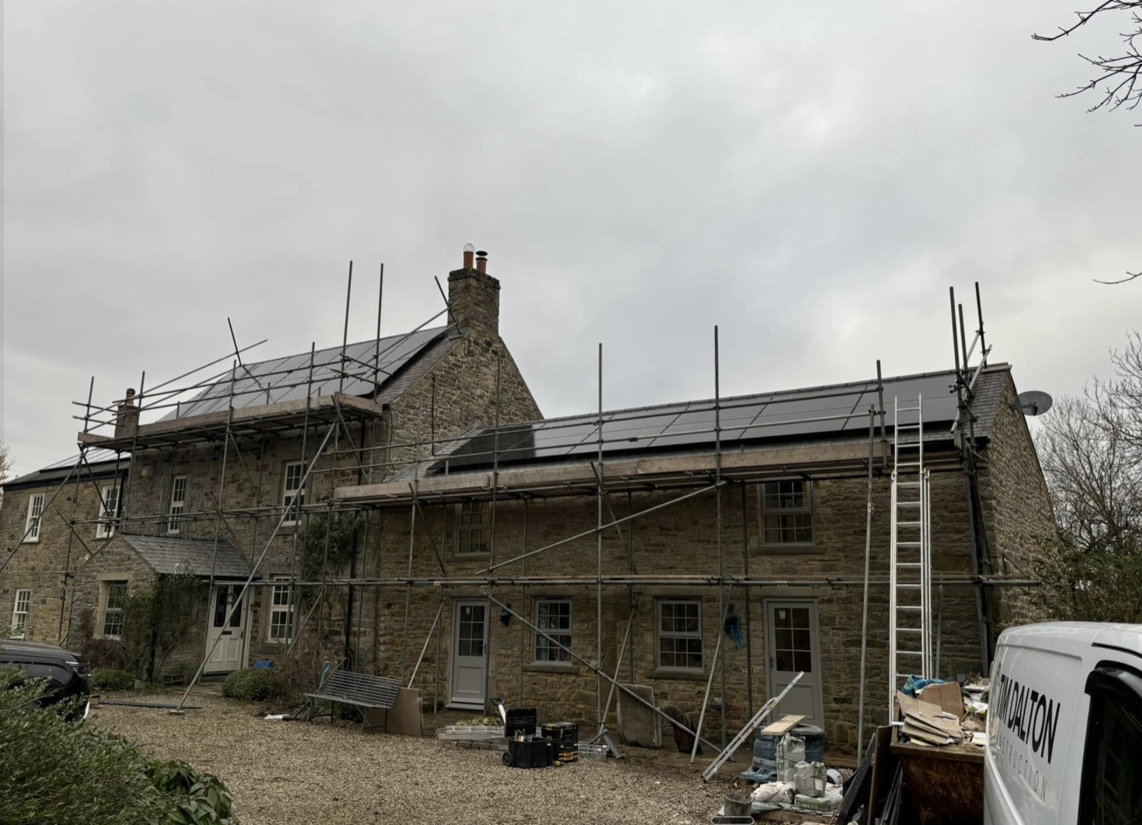 Solar panels across the roof of a scaffolded stone farmhouse