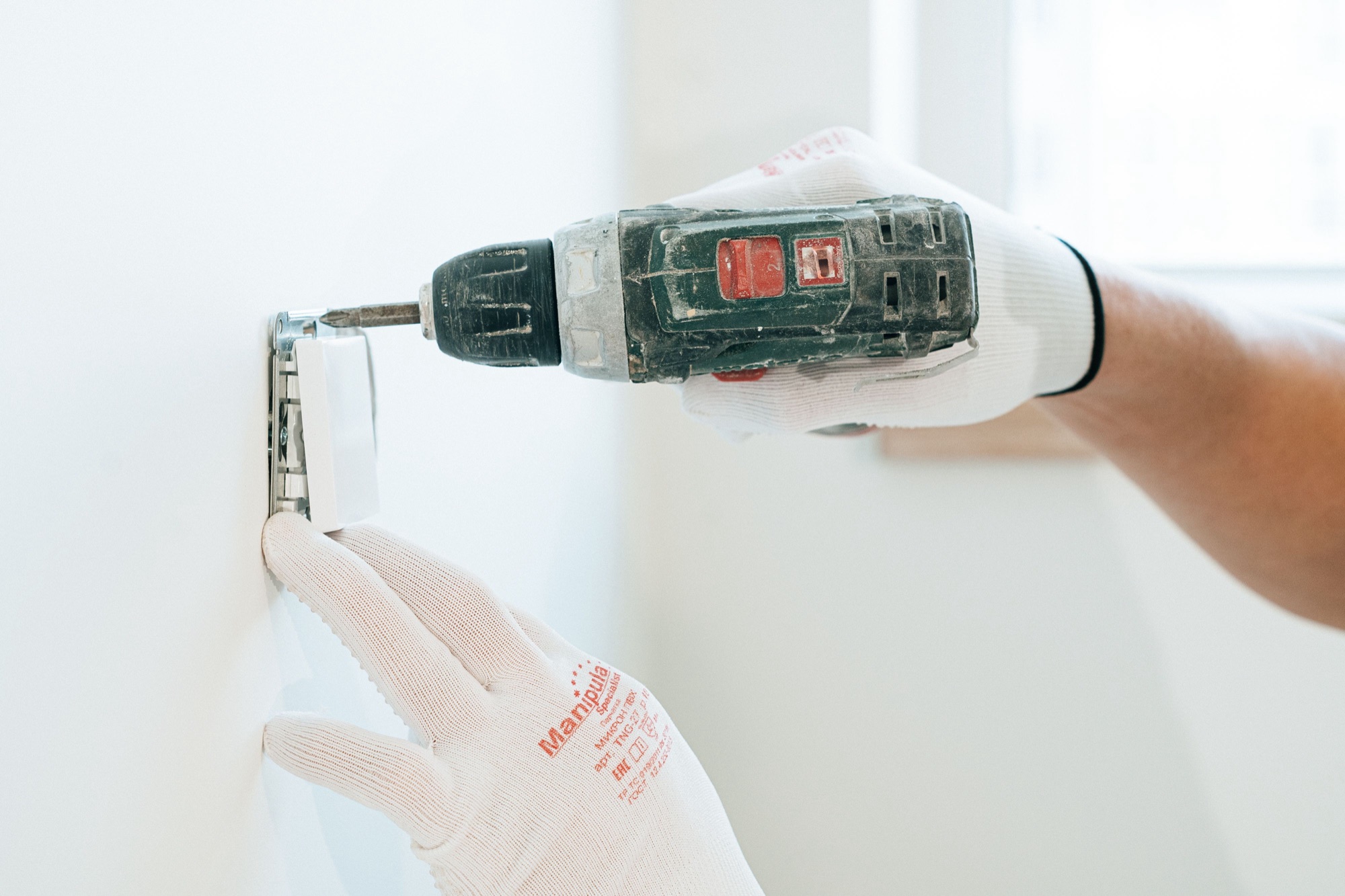 Electrician fixing a socket faceplate to the wall with a cordless drill